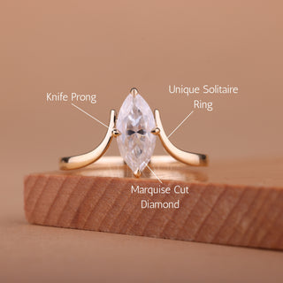 Gold ring with marquise cut diamond on a wooden stand against a brown background